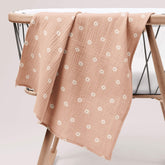 Salmon pink muslin swaddle with white poppy print draped over wooden crib